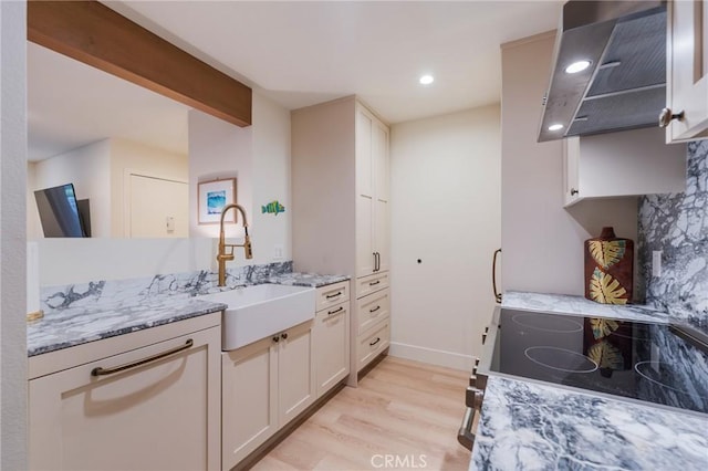 kitchen with a sink, light wood finished floors, light stone counters, electric range oven, and exhaust hood