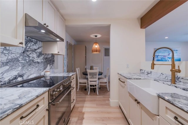 kitchen featuring under cabinet range hood, high end stainless steel range, a sink, light wood-style floors, and light stone countertops