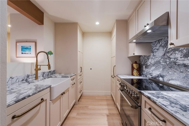 kitchen with stainless steel range, extractor fan, light wood-style flooring, light stone countertops, and backsplash