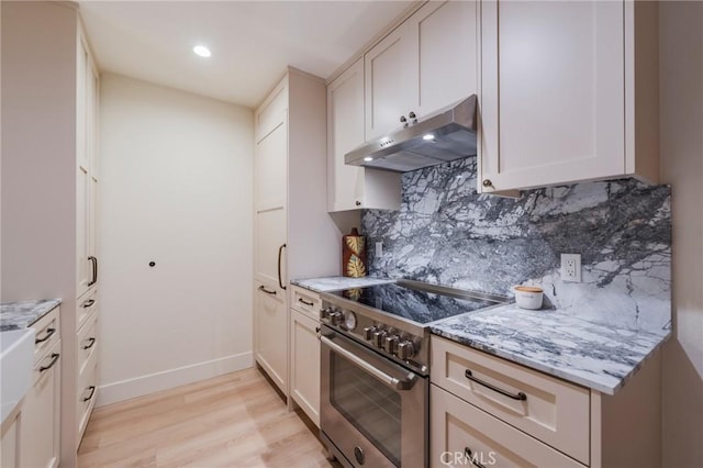kitchen with high end range, under cabinet range hood, light wood finished floors, backsplash, and light stone counters