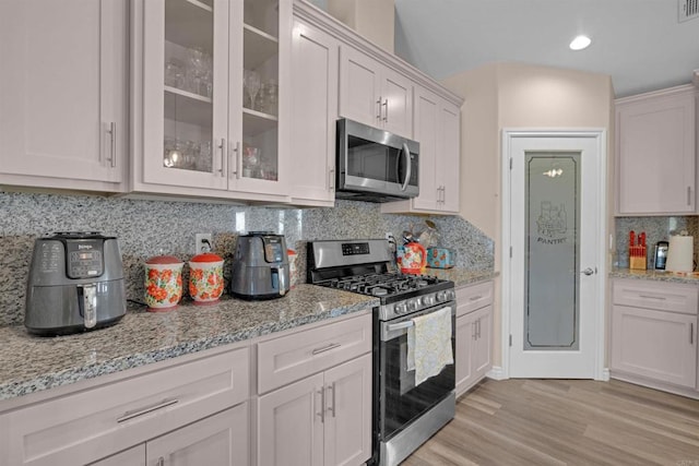 11374 Desert View Rd, Pinon Hills, CA 92372 - kitchen featuring appliances with stainless steel finishes, light stone countertops, glass insert cabinets, decorative backsplash, and light wood-type flooring