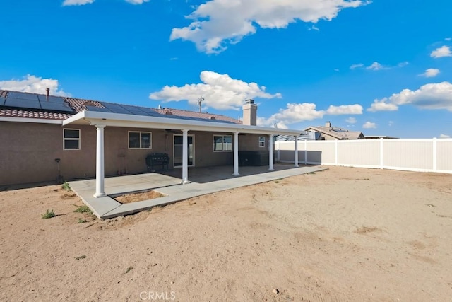 rear view of house featuring solar panels, a fenced backyard, a patio, a chimney, and stucco siding