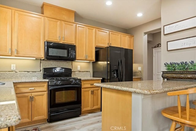 kitchen with black appliances, a kitchen bar, light stone countertops, light wood finished floors, and recessed lighting
