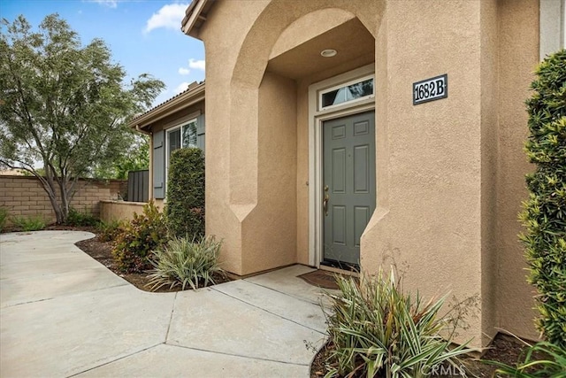 doorway to property with stucco siding, fence, and a patio