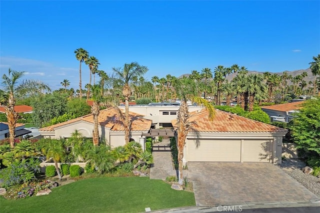 mediterranean / spanish home with a front yard, decorative driveway, stucco siding, a tile roof, and a garage