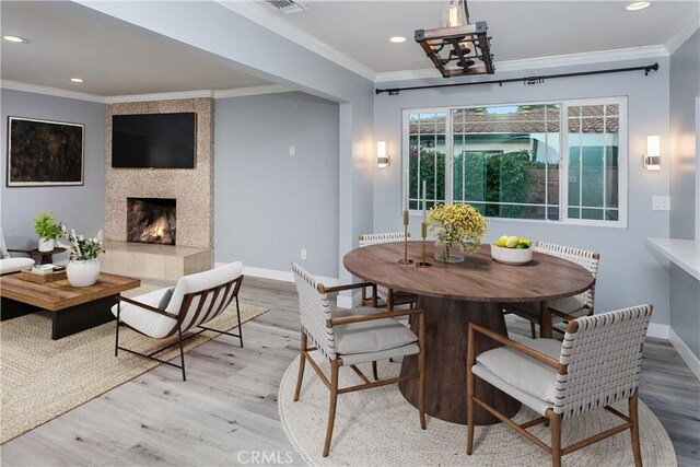 dining area with wood finished floors, recessed lighting, baseboards, crown molding, and a tiled fireplace
