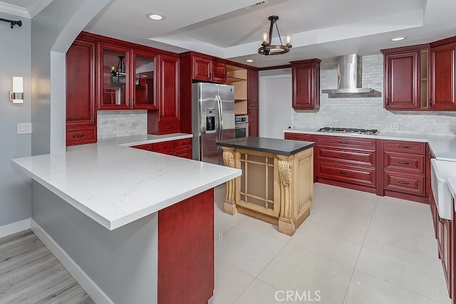 kitchen with wall chimney range hood, dark brown cabinets, a raised ceiling, tasteful backsplash, and recessed lighting