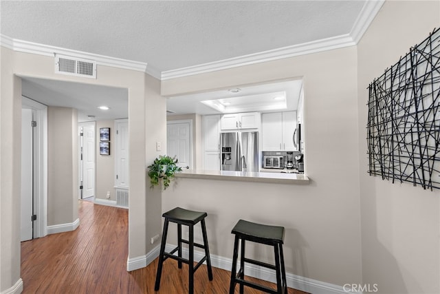 kitchen with appliances with stainless steel finishes, crown molding, a kitchen breakfast bar, white cabinetry, and baseboards