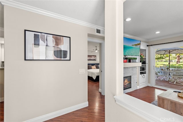 living area with crown molding, wood finished floors, a glass covered fireplace, baseboards, and recessed lighting