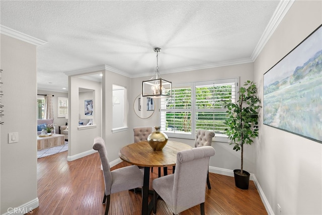 dining room with wood finished floors, a textured ceiling, crown molding, a chandelier, and baseboards