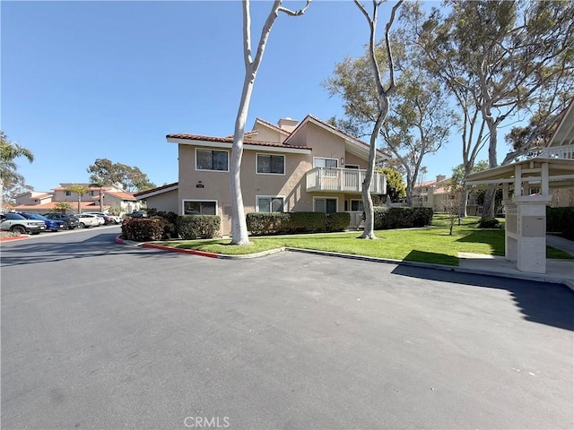 view of front of property featuring stucco siding, a front lawn, a tile roof, and uncovered parking