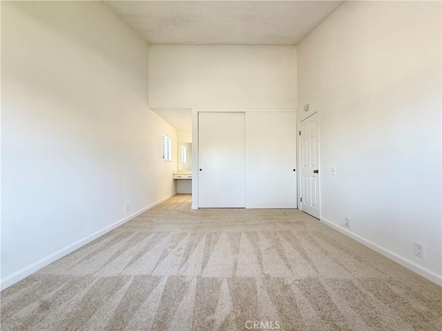 unfurnished bedroom featuring a towering ceiling, carpet flooring, a closet, and baseboards