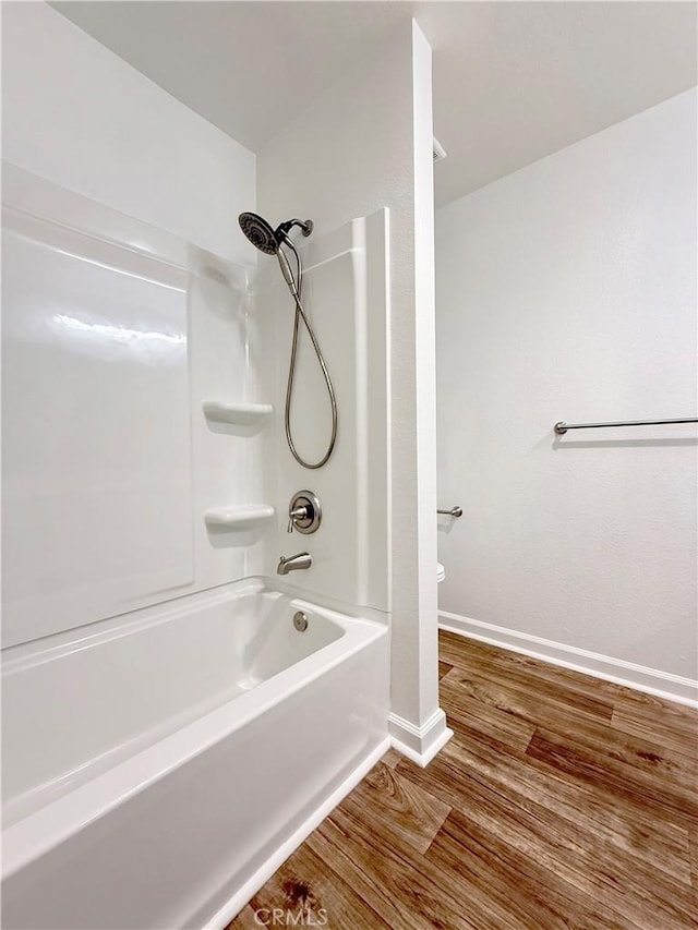 bathroom featuring wood finished floors, baseboards, shower / bathtub combination, and toilet
