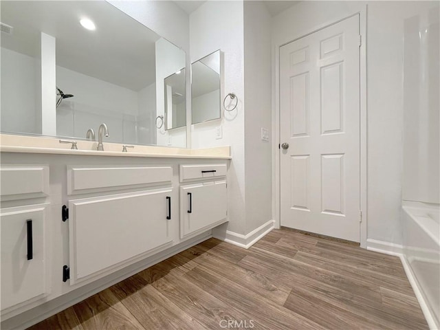 bathroom featuring baseboards, wood finished floors, vanity, a tub to relax in, and recessed lighting