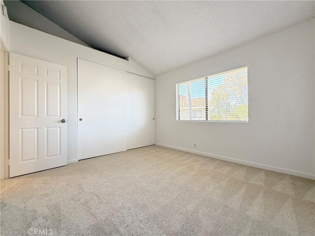 empty room with lofted ceiling, carpet flooring, a textured ceiling, and baseboards