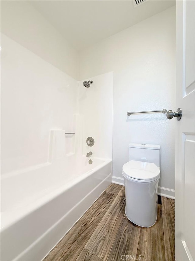 full bathroom with wood finished floors, baseboards, toilet, and washtub / shower combination