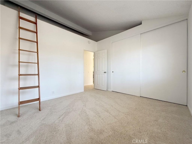 unfurnished bedroom with carpet, lofted ceiling, a closet, and baseboards