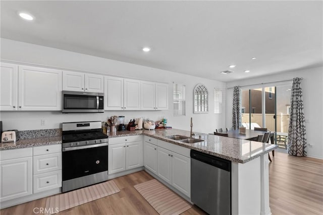 kitchen with appliances with stainless steel finishes, a sink, a peninsula, light wood-style flooring, and white cabinets