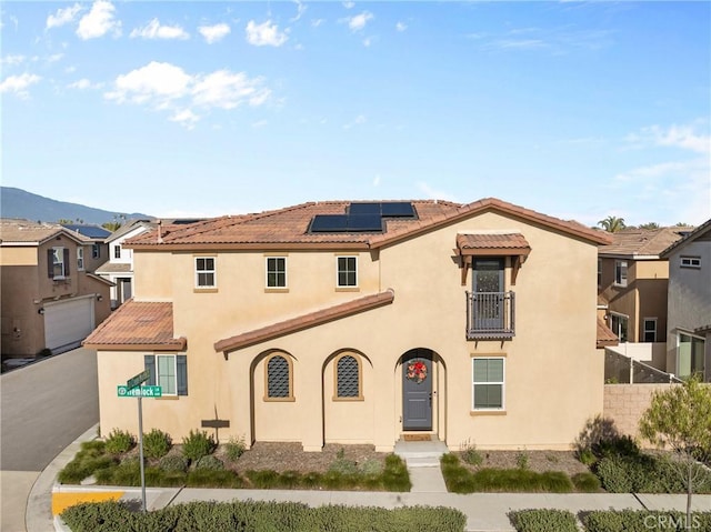 mediterranean / spanish-style house with roof mounted solar panels, a tiled roof, stucco siding, fence, and a mountain view