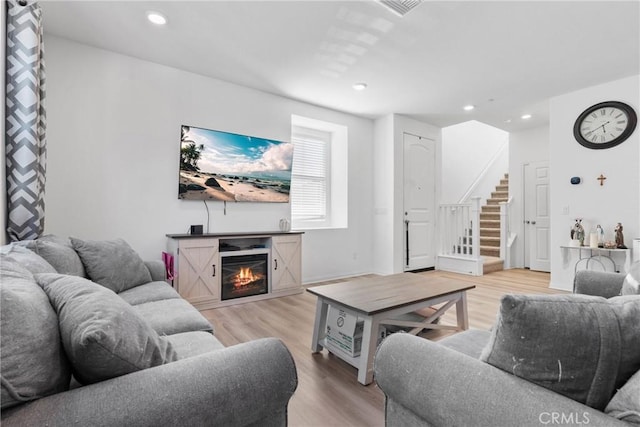 living area featuring stairs, light wood-type flooring, recessed lighting, and a glass covered fireplace