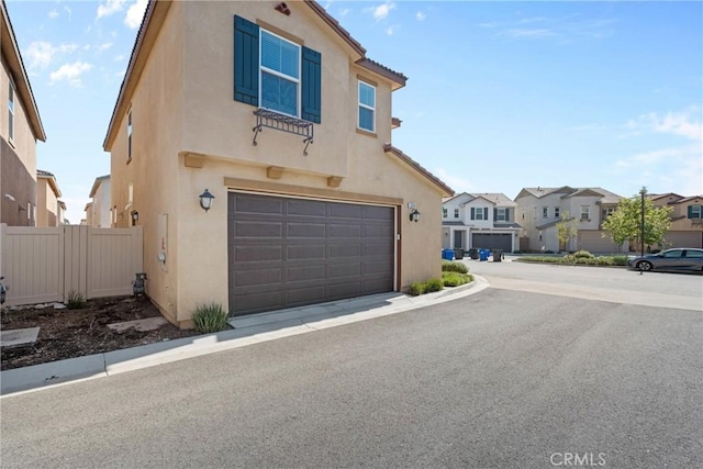 view of front of home featuring stucco siding, a garage, a residential view, and fence