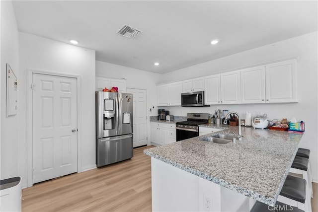 kitchen with appliances with stainless steel finishes, a sink, white cabinetry, a kitchen breakfast bar, and recessed lighting
