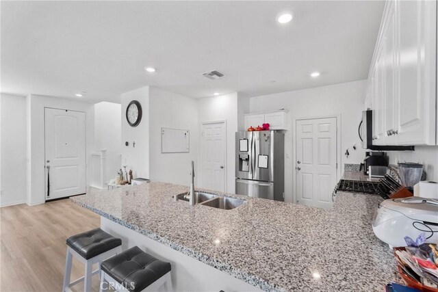 kitchen with stainless steel appliances, a sink, light stone countertops, a peninsula, and white cabinets