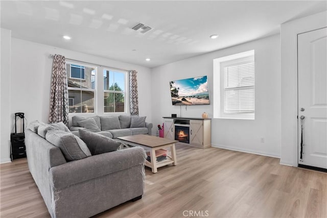 living room with light wood finished floors, a lit fireplace, baseboards, and recessed lighting