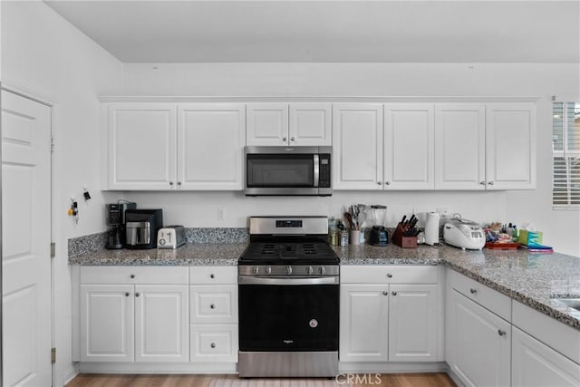 kitchen featuring appliances with stainless steel finishes, white cabinetry, and light stone counters