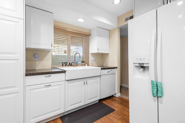 kitchen with a sink, white appliances, light wood-type flooring, visible vents, and white cabinetry