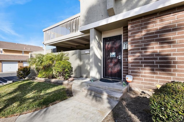 entrance to property with brick siding, stucco siding, and a balcony