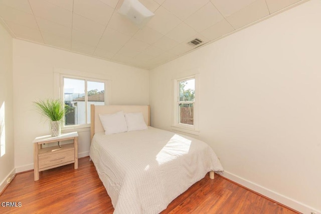 bedroom with multiple windows, wood finished floors, and baseboards