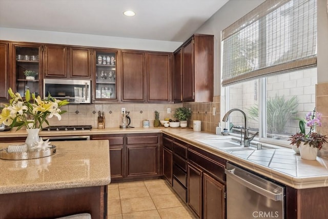 kitchen with stainless steel appliances, a sink, tasteful backsplash, light tile patterned floors, and open shelves