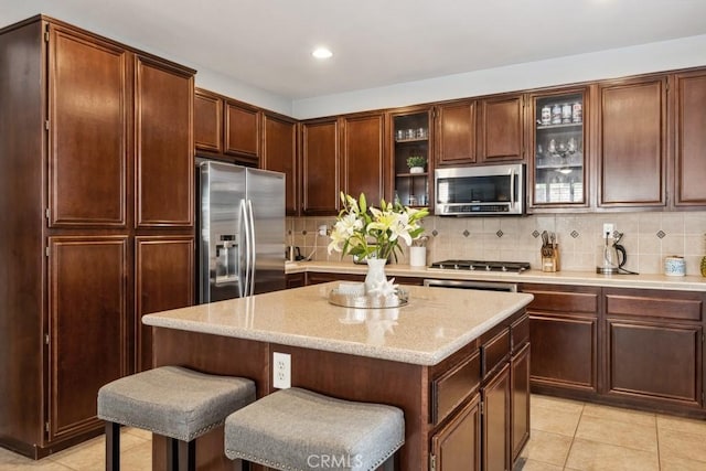 kitchen with stainless steel appliances, a kitchen island, backsplash, glass insert cabinets, and recessed lighting