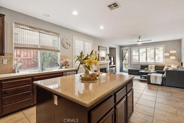 kitchen featuring a sink, a fireplace, light tile patterned floors, a kitchen island, and dishwasher