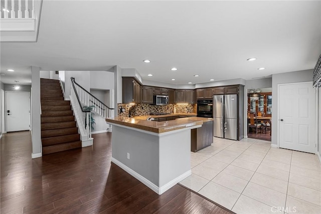 26426 Cardinal Dr, Canyon Country, CA 91387 - kitchen with stainless steel appliances, dark brown cabinets, a peninsula, decorative backsplash, and light wood finished floors