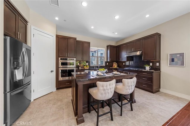124 Trumpet Flower, Irvine, CA 92618 - kitchen featuring stainless steel appliances, dark brown cabinets, under cabinet range hood, a breakfast bar area, and tasteful backsplash