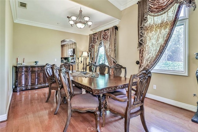 dining room with a chandelier, arched walkways, baseboards, wood finished floors, and ornamental molding
