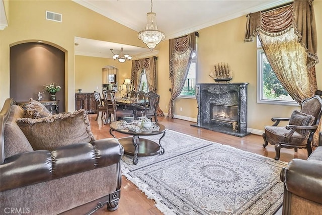living area with ornamental molding, a chandelier, wood finished floors, a fireplace, and vaulted ceiling