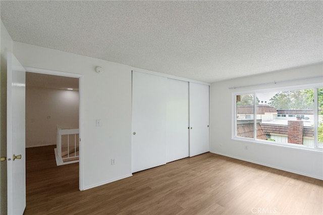 unfurnished bedroom with wood finished floors, a textured ceiling, a closet, and baseboards