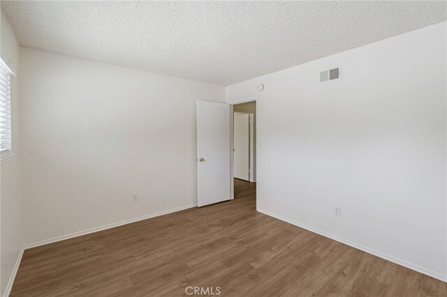 unfurnished room with wood finished floors, a textured ceiling, and baseboards