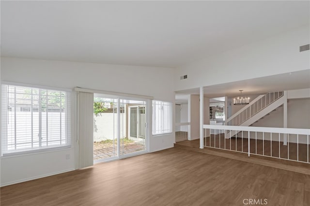 unfurnished living room with wood finished floors, a chandelier, vaulted ceiling, and baseboards
