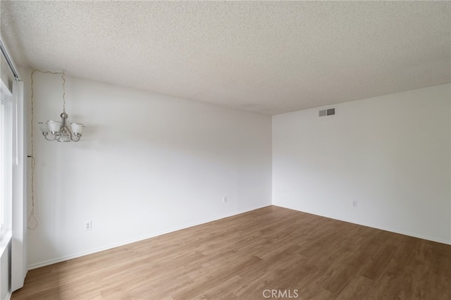 spare room featuring a chandelier, light wood finished floors, and a textured ceiling