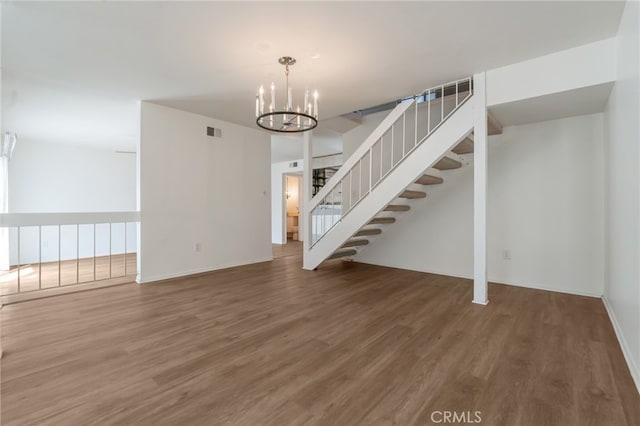 unfurnished living room featuring wood finished floors, a chandelier, and stairway