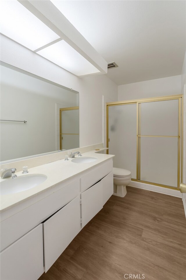 full bath featuring a stall shower, double vanity, wood finished floors, and toilet