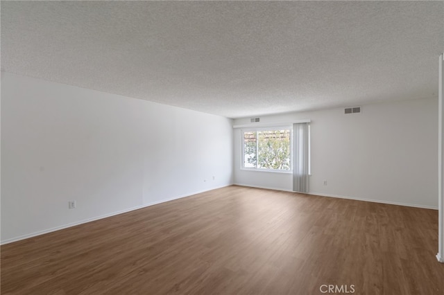 empty room with wood finished floors, a textured ceiling, and baseboards