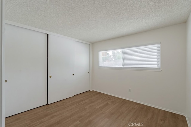 unfurnished bedroom featuring light wood-style floors, a closet, a textured ceiling, and baseboards