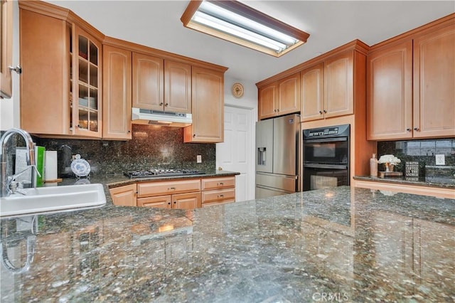 kitchen featuring stainless steel refrigerator with ice dispenser, under cabinet range hood, gas stovetop, a sink, and glass insert cabinets