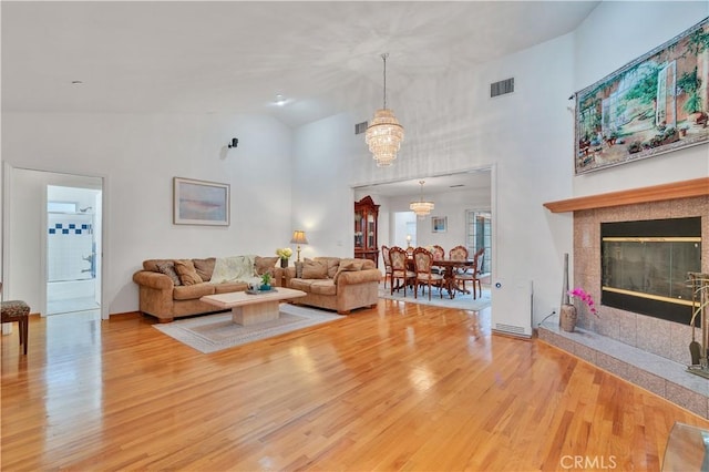 living room featuring high vaulted ceiling, wood finished floors, a tile fireplace, and a chandelier