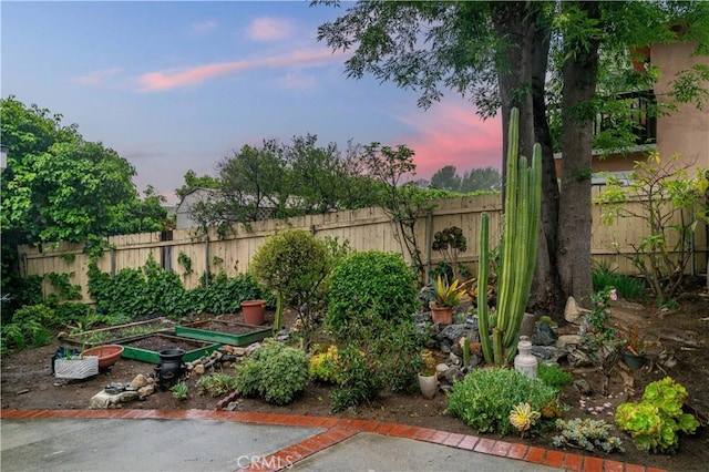 yard at dusk featuring a vegetable garden and fence